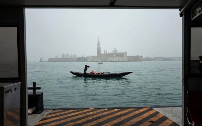 Un gondolero viaja en su barca vacía a través de la cuenca de San Marco con la iglesia de San Giorgio Maggiore, como fondo, en Venecia.