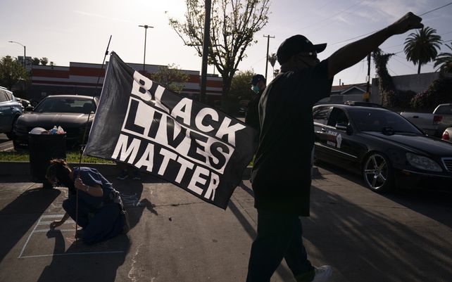 Una mujer con una bandera de Black Lives Matter escribe un mensaje en una acera en Los Ángeles