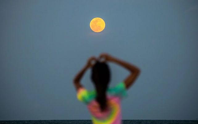 Una luna llena súper rosa se ve en el fondo en una playa de Miami Beach.