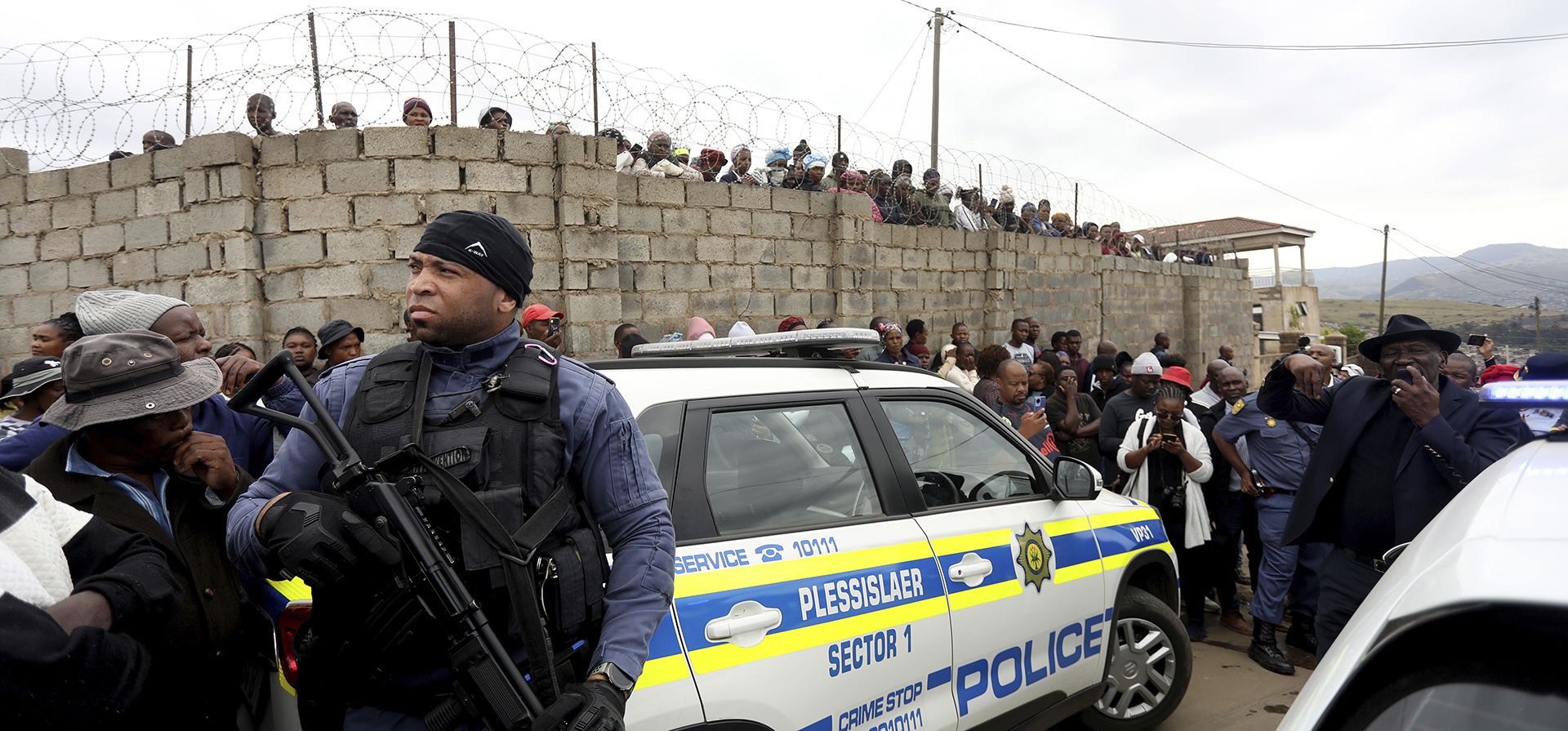 La gente se agolpa detrás de un cordón policial, donde diez personas de la misma familia fueron asesinadas a tiros el viernes 21 de abril de 2023. La policía dice que 10 personas fueron "emboscadas" por desconocidos armados en una casa en la ciudad de Pietermaritzburg, en la provincia oriental de KwaZulu-Natal , Sudáfrica. (Foto AP)