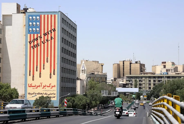 Coches circulan junto a un edificio que muestra un mural contra Estados Unidos en Teherán