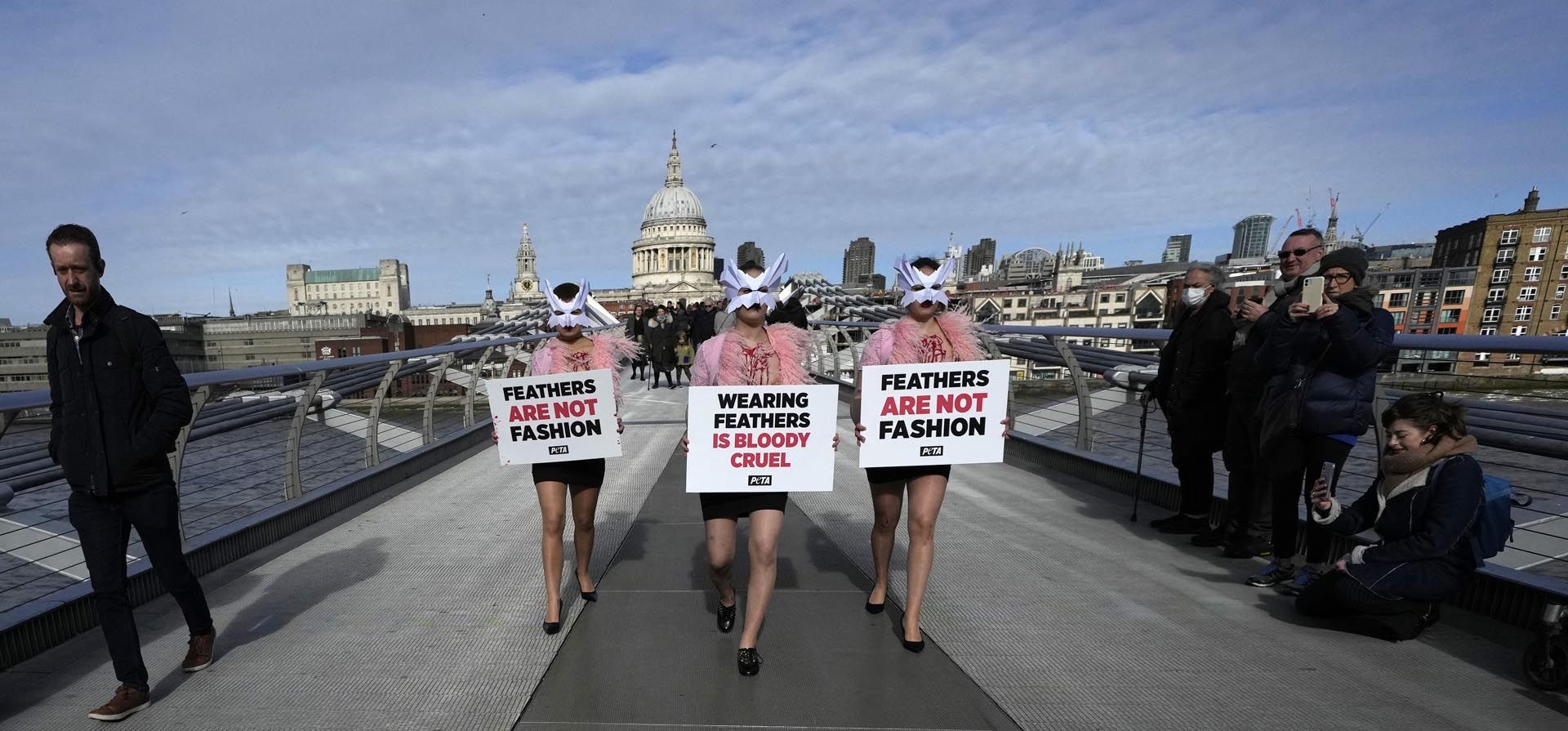 Manifestantes de PETA ( organizacion defensora de los derechos de los animales) sostienen pancartas durante una manifestación contra el uso de plumas, en la Semana de la Moda de Londres, en el Puente del Milenio con la Catedral de San Pablo en el fondo en Londres, el jueves, febrero 17 de 2022.