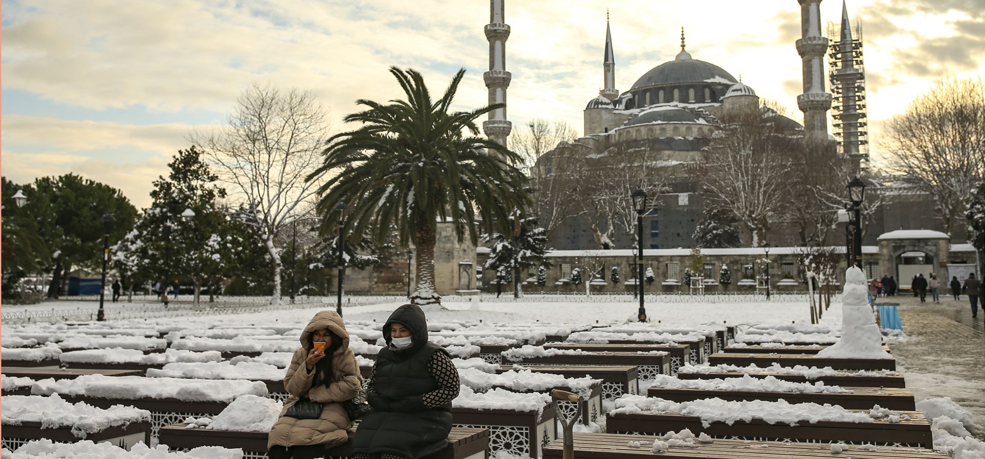 Dos mujeres descansan en un parque cubierto de nieve con el Sultán Ahmed o la Mezquita Azul detrás en Estambul. Los equipos de rescate en despejaron las carreteras que se habían paralizado después de un frente frío masivo.